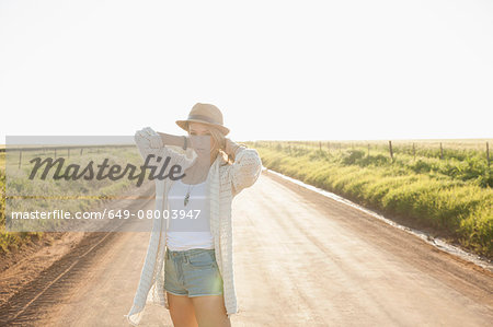 Mid adult woman on country road, arms behind neck, looking at camera