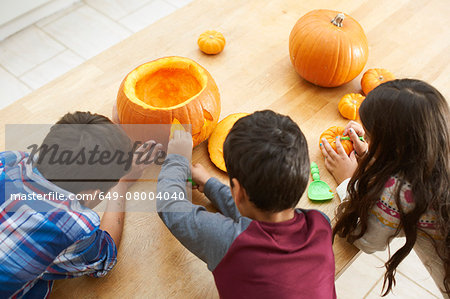 Siblings carving pumpkin in dining room