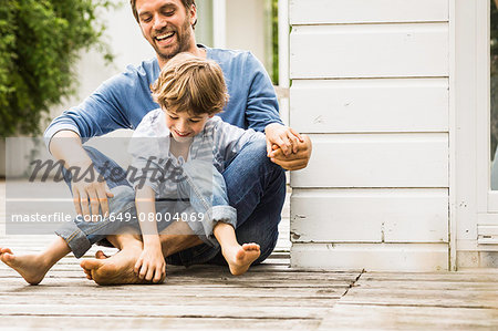 Mid adult man and son laughing and tickling feet on porch