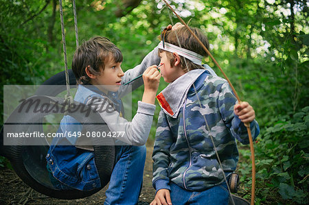 Boy face painting friend whilst playing in forest