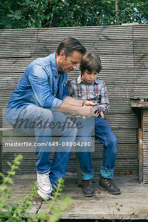 Father showing son how to use pocket knife on allotment