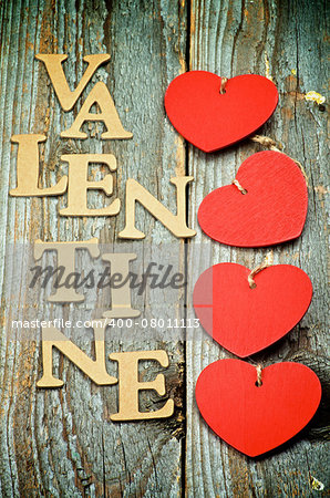 Four Red Hearts In a Row and Cardboard Words Valentine on Rustic Wooden background