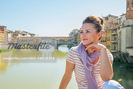 Young woman sitting on bridge overlooking ponte vecchio in florence, italy and looking into distance
