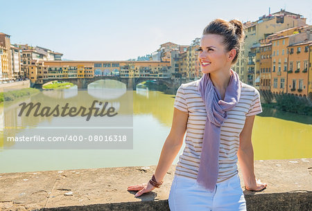 Happy young woman sitting on bridge overlooking ponte vecchio in florence, italy and looking into distance