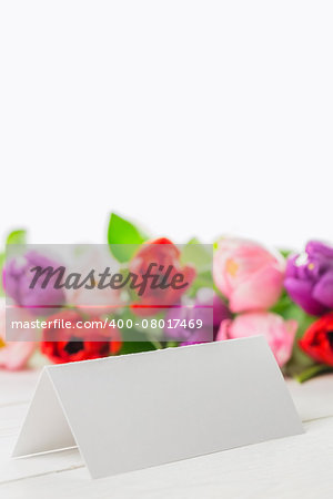 Colorful tulips and white card on wooden table