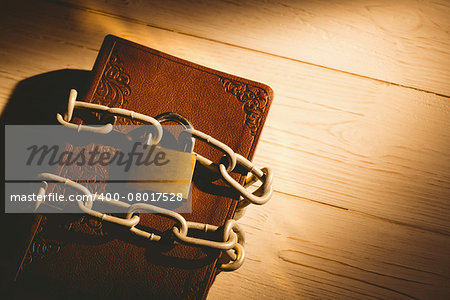 Open bible chained with lock on wooden table