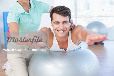 Trainer with man on exercise ball in fitness studio