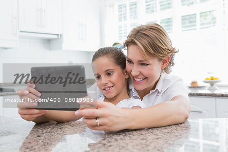 Mother and daughter using tablet pc at home in kitchen