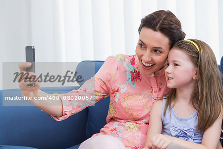 Mother and daughter taking selfie at home in the living room