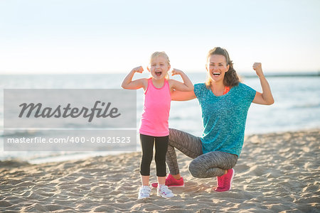 Healthy mother and baby girl showing biceps on beach