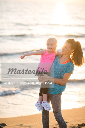 Healthy mother and baby girl pointing while on beach in the evening