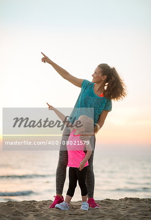 Healthy mother and baby girl on beach in the evening pointing