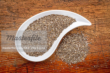 chia seeds in a teardrop shaped bowl - top view against rustic wood