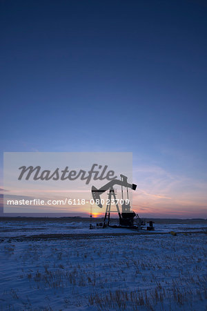 An oil drilling rig and pumpjack on a flat plain in the Canadian oil fields at sunset. An oil drilling rig and pumpjack on a flat plain in the Canadian oil fields at sunset.