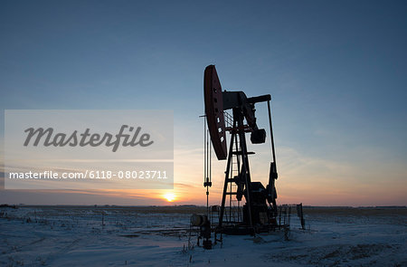 An oil drilling rig and pumpjack on a flat plain in the Canadian oil fields at sunset.