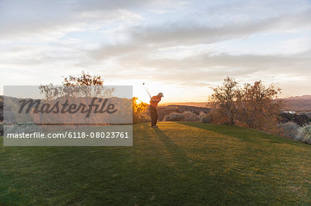A man taking a shot off a golf tee on a golf course into the sunset.