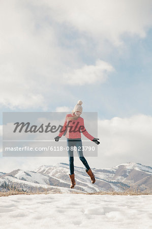 A young girl with long legs and red jacket, leaping in the air above the snow