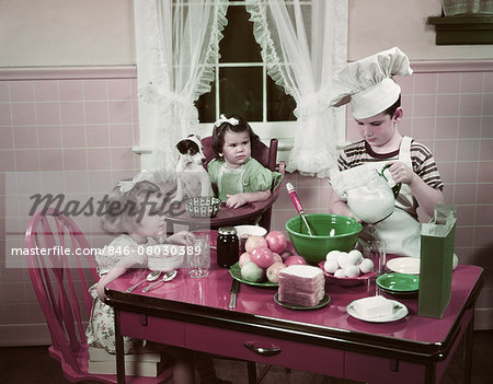 1940s 1950s BOY TWO GIRLS AT KITCHEN TABLE BOY IN TOQUE COOKING ONE GIRL EATING TODDLER AND PUPPY IN HIGH CHAIR