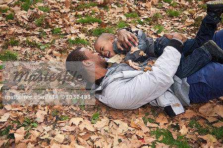 Young man and toddler son lying in autumn leaves in park