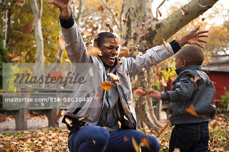 Young man and toddler son throwing autumn leaves in park