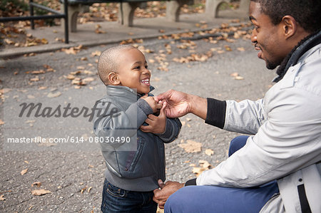 Male toddler fastening jacket zipper in park