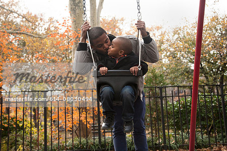 Male toddler and father on park swings