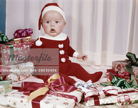 1960s AMAZED BABY IN SANTA SUIT SITTING AMONG WRAPPED PRESENTS