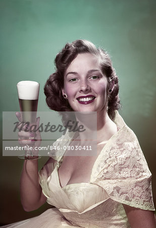 1950s PORTRAIT SMILING WOMAN WEARING FORMAL GOWN HOLDING PILSNER GLASS OF BEER LOOKING AT CAMERA