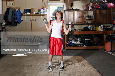 Slim boy struggling to lift hand weights in garage