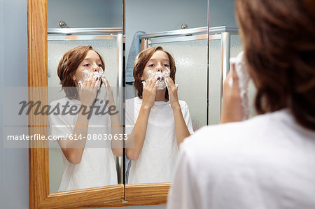 Boy practicing applying shaving foam in bathroom mirror