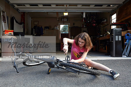 Girl repairing bicycle in front of garage