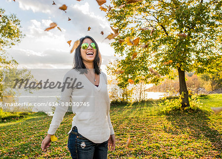 Mid adult woman smiling, autumn leaves falling