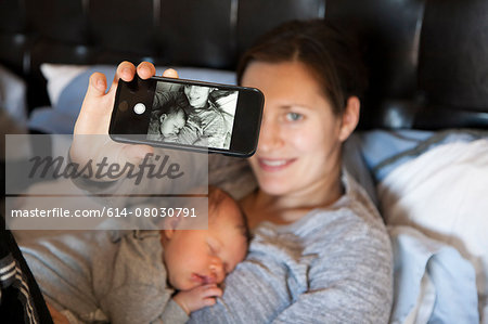 Baby girl sleeping on mother's chest, while mother takes self portrait of them both, using smartphone