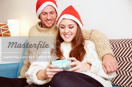 Young couple in santa hats on sofa looking down at christmas gift