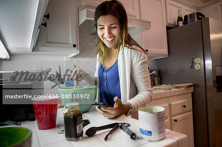 Woman preparing food in kitchen whilst reading recipe from smartphone