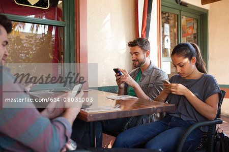 Four friends individually texting on smartphones in vegetarian restaurant