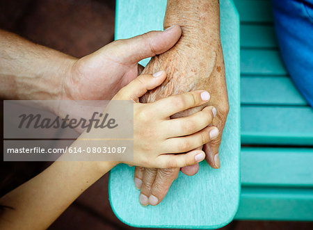 Cropped close up of senior woman, son and grandson hands touching in park