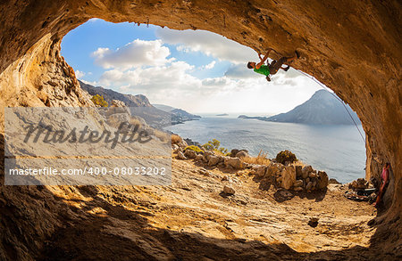 Young man lead climbing in cave with beautiful view in background