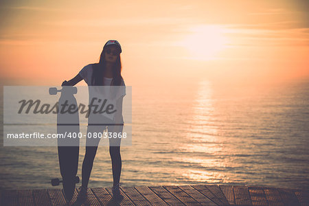 Beautiful fashion skater girl posing with  a skateboard at the sunset