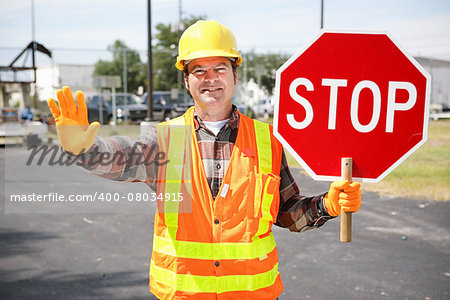 Friendly construction worker in the road holding up a stop sign.