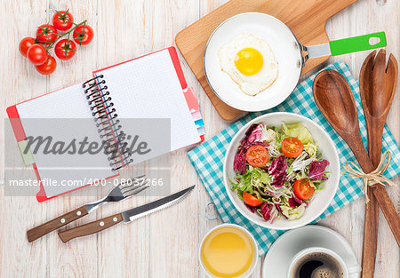 Healthy breakfast with fried egg, toasts and salad on white wooden table with notepad for copy space