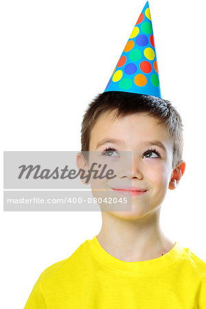 Portrait of eight years boy with birthday cap looking up on white background