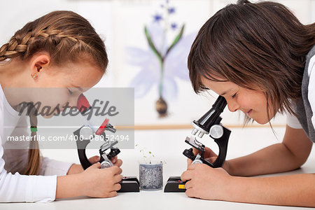 Young kids in science lab study samples under the microscope - biology class
