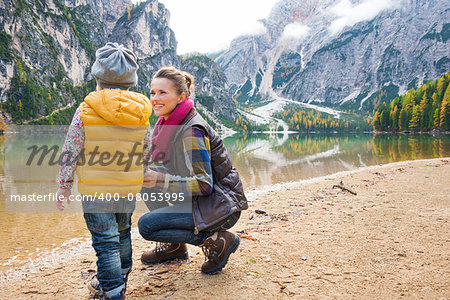 Dressed in outdoors gear a mother is smiling at her daughter. Seen from behind, the daughter looks out at the trees, mountains, and fall colours in the reflections on the water.
