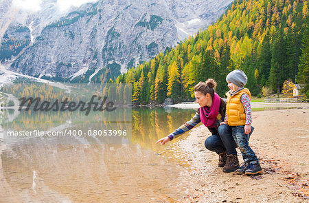 A mother, kneeling next to her daughter on the shores of Lake Bries, is pointing into the water. The colours of their hiking gear reflect the autumn foliage.