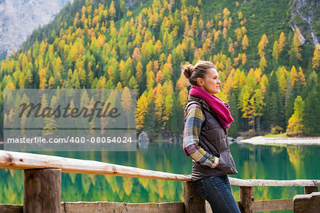 A brunette hiker wearing outdoor gear stands thinking on the shores of Lake Bries. The still water, golden colours and shades of gray provide an autumn background that is reflected in the still water.