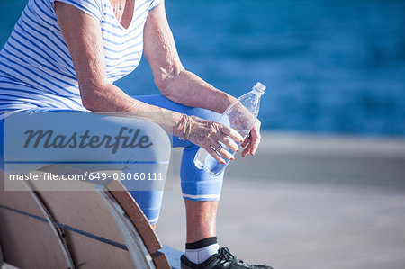 Senior woman sitting on bench by sea holding bottled water
