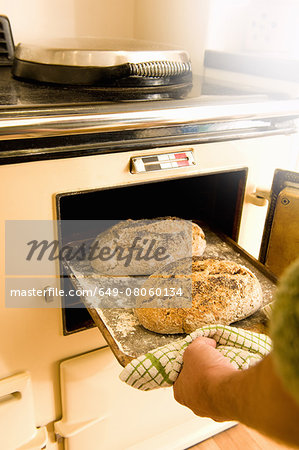 Mature man taking baking tray with fresh bread from oven