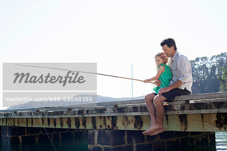 Mature man and daughter fishing on sea pier, New Zealand