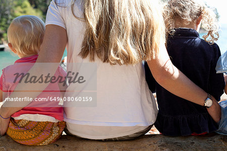 Rear view of mother and two daughters sitting on tree trunk at beach, New Zealand